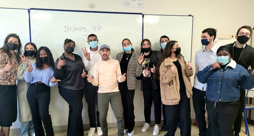 Groupe d'étudiants et intervenant réunis à l'issue d'un atelier, devant un tableau où est écrit « Stand-up »